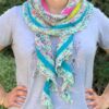 A close up of a white woman wearing a pale grey tshirt with a striped knitted shawl wrapped around her neck