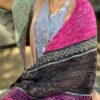 A white woman wearing a pale grey tshirt sits on an old wooden bench, her face is out of view. She has a colourful knitted shawl draped across one shoulder to show the chevron stripes and patterns in the knitting