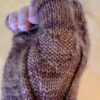 A close-up of the thumb portion of a brown knitted mitten showing a heart shape hidden in the stitches