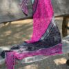 An asymmetrical triangle shaped knitted shawl lies draped across an old wooden bench as the sun makes shadows across the surface of the stitches