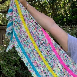 A white woman stretches out her arm to show the end of a colourful knitted shawl