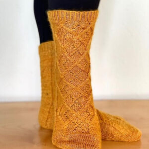 A close up view of a knitted gold sock showing the pattern of lace and cable stitches in a diamond pattern