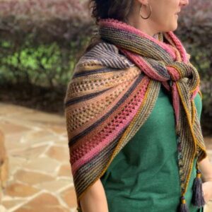 A white woman wears a brightly coloured rainbow knitted shawl tied around her neck