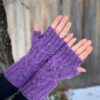 White hands are wearing purple knitted mittens and are held palms up to show the cable design of the mitts