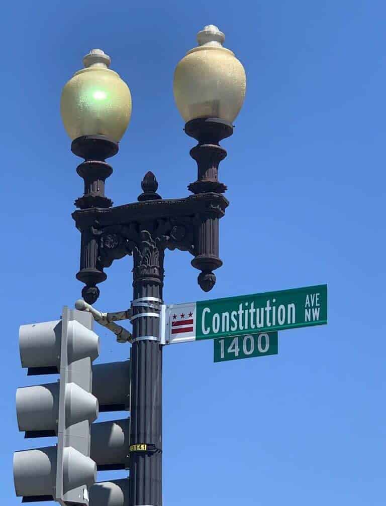 An ornate lampost with a street sign reading Constitution Avenue 1400 Block is pictured against a dark blue sky