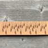 A close-up view of a natural undyed leather cuff on a grey wooden surface. There is a design etched onto the cuff showing thirty-three tiny feathers hanging from strings.